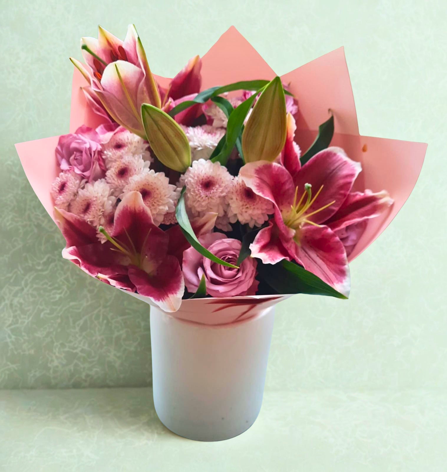 Pink bouquet featuring 2 lilies, 3 chrysanthemums, and 10 roses with fresh greenery, elegantly wrapped in pink paper.